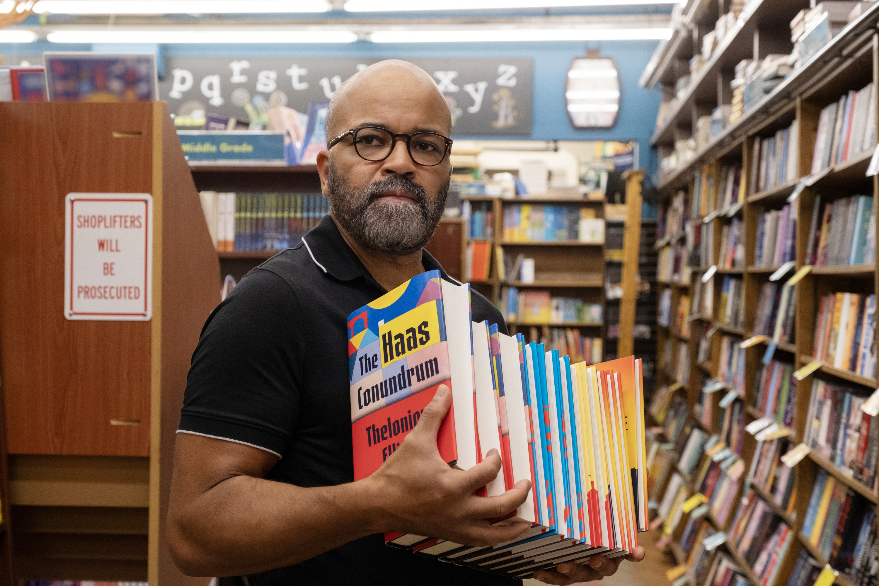 Jeffrey Wright holding a stack of books in a bookstore.